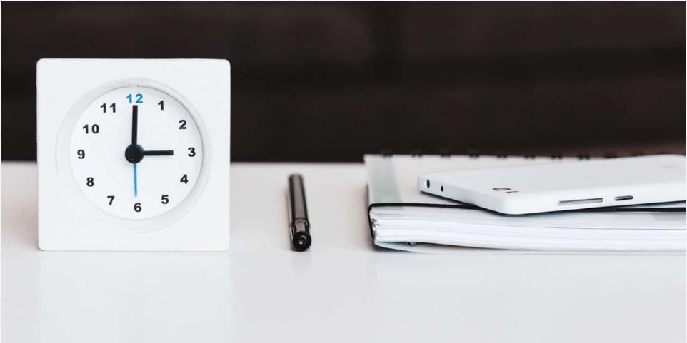 Clock with pen and phone on table